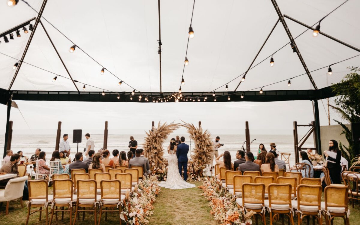 Casamento à beira-mar em Capão da Canoa com casal trocando alianças ao entardecer dourado, cercado por vegetação natural e vista para o oceano