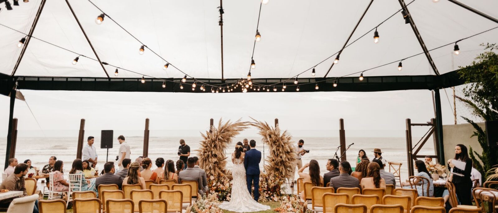 Casamento à beira-mar em Capão da Canoa com casal trocando alianças ao entardecer dourado, cercado por vegetação natural e vista para o oceano