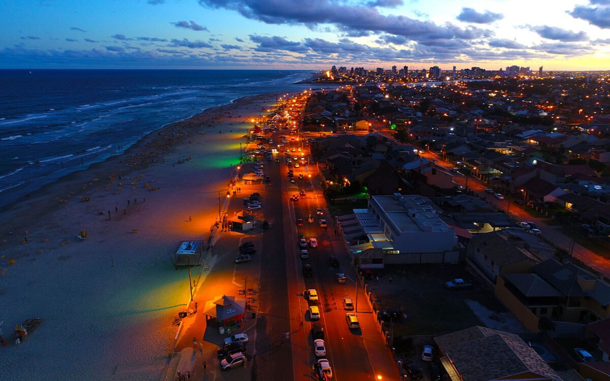 Vista aérea da praia de Capão da Canoa ao pôr do sol com resort à beira-mar, mostrando o que fazer em Capão da Canoa durante hospedagem
