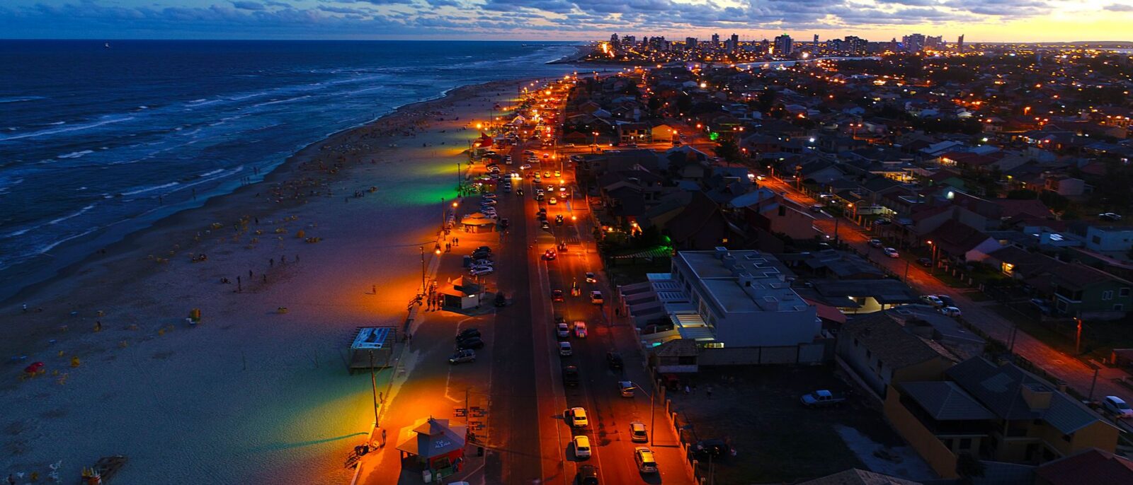 Vista aérea da praia de Capão da Canoa ao pôr do sol com resort à beira-mar, mostrando o que fazer em Capão da Canoa durante hospedagem